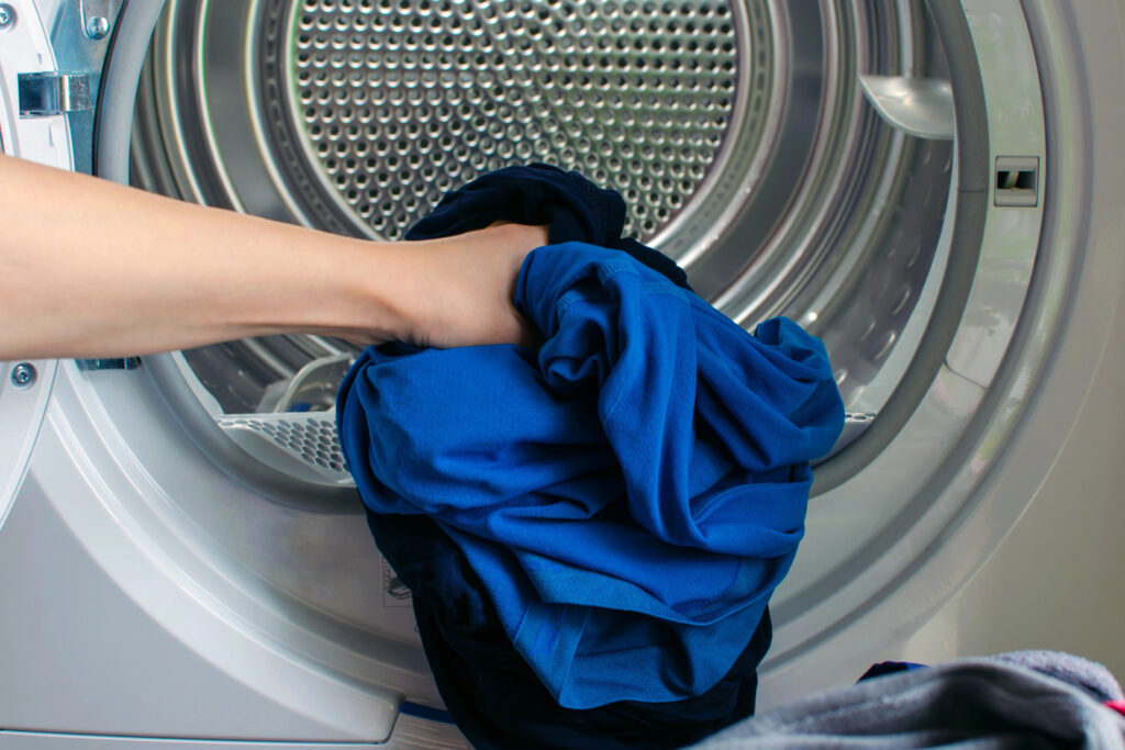 Hand legt blaue Arbeitskleidung in eine industrielle Waschmaschine bei Masterdress